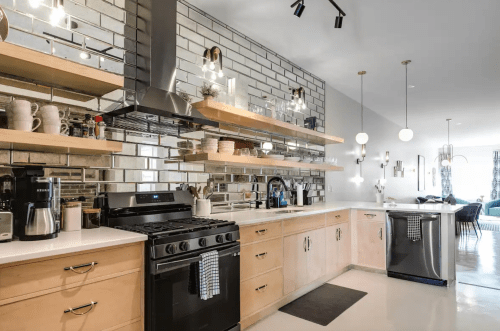 Modern kitchen with stainless steel appliances, open shelving, and a sleek design featuring light wood and gray tiles.