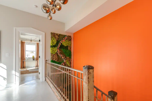Bright hallway featuring an orange wall, modern light fixture, and a green moss art piece.
