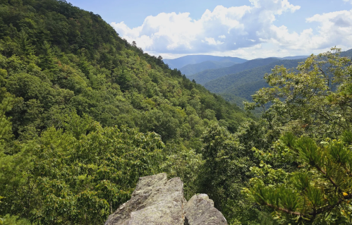 A scenic view of lush green mountains under a bright blue sky with fluffy clouds.
