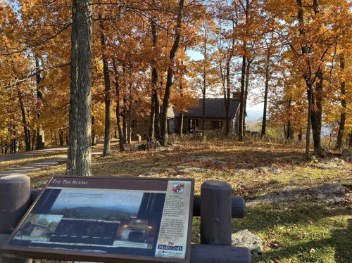 A wooden sign in front of a rustic cabin surrounded by vibrant autumn foliage and trees.