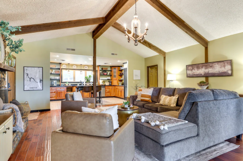 Cozy living room with vaulted ceiling, wooden beams, and comfortable seating, leading to a kitchen area in the background.