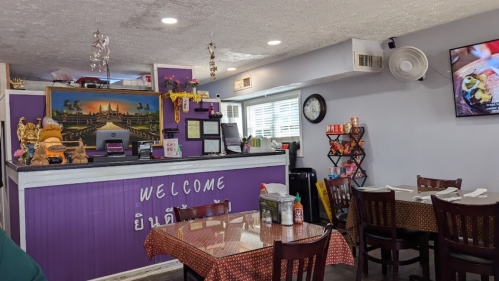 Interior of a cozy restaurant with purple walls, a welcoming counter, and tables set for dining.