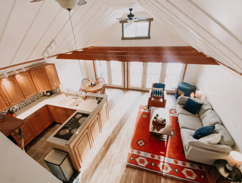 Bright, airy living space with a kitchen, dining area, and cozy seating, featuring wooden beams and large windows.