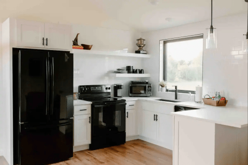 Modern kitchen featuring black appliances, white cabinets, open shelving, and a large window with a view.
