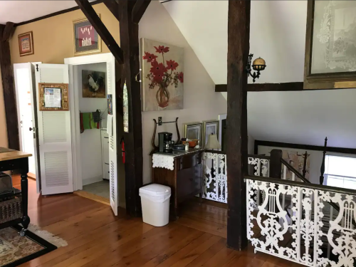 A cozy interior with wooden beams, a staircase, and decorative art on the walls, featuring a coffee station and a white railing.