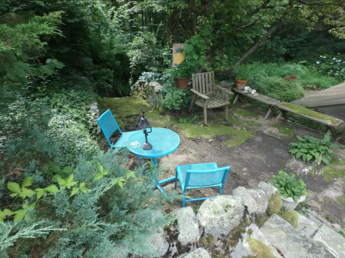 A serene garden scene featuring a blue table and chairs surrounded by lush greenery and stone pathways.