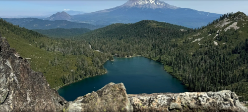 A scenic view of a mountain landscape featuring a lake surrounded by forests and distant peaks.