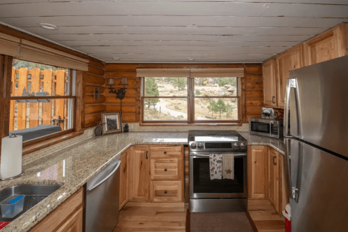Cozy kitchen with wooden cabinets, granite countertops, and large windows overlooking a scenic outdoor view.