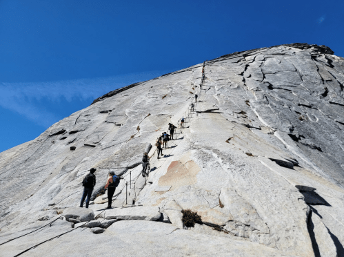 Hikers ascend a steep, rocky slope with a clear blue sky above, showcasing a challenging outdoor adventure.