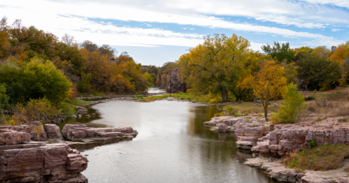 Winding Split Rock Creek flows through a landscape of large, flat, pink Sioux Quartzite rocks and colorful fall foliage.