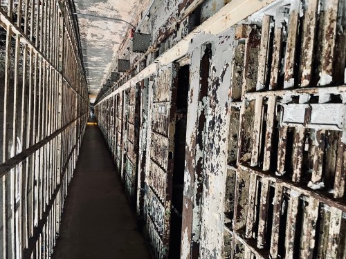 A dimly lit prison corridor lined with old, rusty cell doors and peeling paint on the walls.