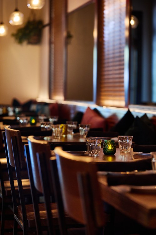 Cozy restaurant interior with wooden tables, glassware, and soft lighting, featuring colorful candles and plush seating.