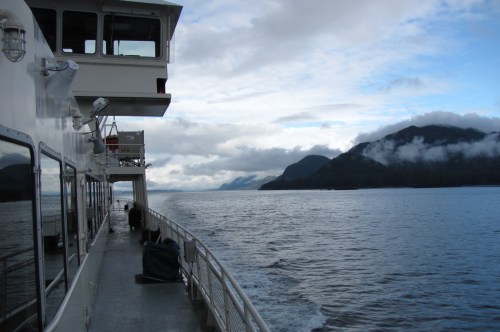 A ferry deck with a view of mountains and cloudy skies over calm waters.