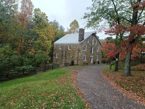 A stone house surrounded by colorful autumn trees and a gravel path, set in a serene, wooded area.