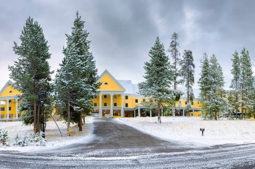 A yellow hotel surrounded by snow-covered trees and a snowy pathway under a cloudy sky.