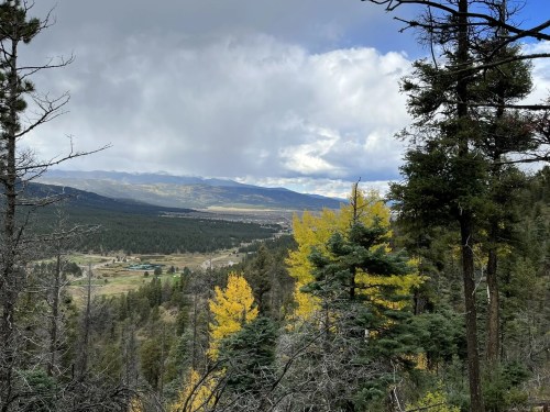 A scenic view of mountains and valleys, with autumn foliage in the foreground and cloudy skies above.