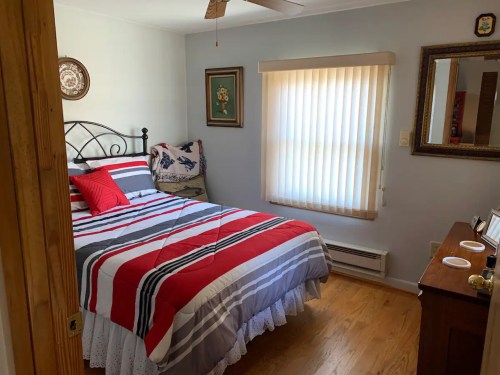 Cozy bedroom with a striped red and gray bedspread, wooden furniture, and a window with blinds.