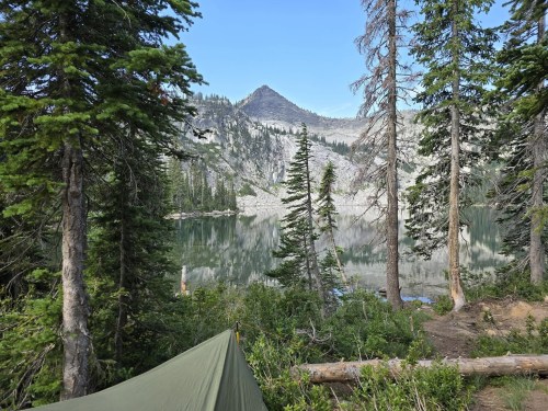 A serene lake surrounded by tall trees and mountains, with a tent set up in the foreground.