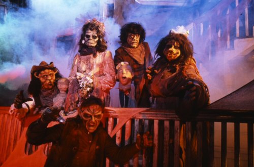 A group of spooky, costumed figures with eerie makeup poses in a foggy, haunted setting.