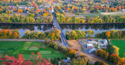 aerial shot of the connecticut river valley with farmland greenery on one side of the river and fall foliage in the town of amherst on the other in western massachusetts