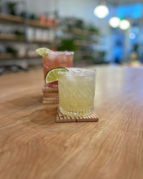 Two colorful cocktails on a wooden table, one with a lime wedge, in a bright, inviting setting.