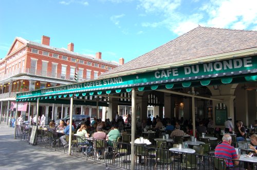 Outdoor seating at Café du Monde, bustling with patrons enjoying coffee and beignets in a lively market setting.