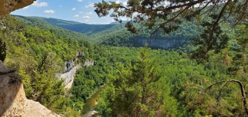 A lush green valley with a winding river, surrounded by steep cliffs and mountains under a clear blue sky.
