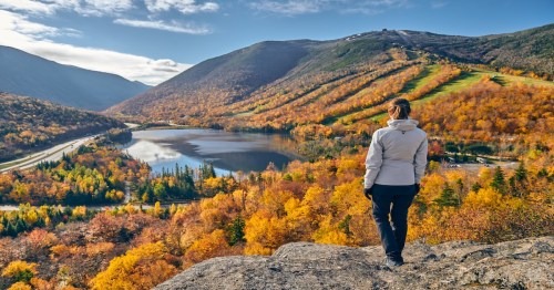 Woman hiking at Artist's Bluff in autumn. View of Echo Lake. Fall colours in Franconia Notch State Park.