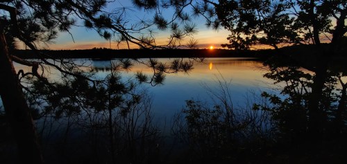 A serene lake at sunset, with silhouettes of trees and colorful reflections on the water's surface.