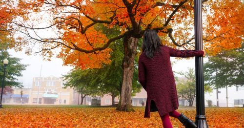 A woman standing in a town square in Arkansas, surrounded by vibrant fall foliage