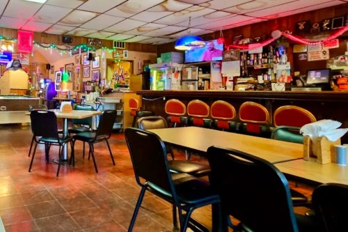 Cozy restaurant interior with empty tables, a bar area, and colorful lights decorating the walls.