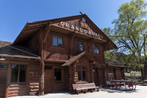 Historic Grand Canyon building with wooden architecture, large windows, and a sign, surrounded by trees and blue sky.