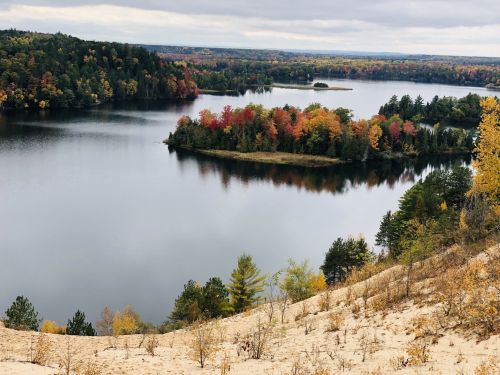 A serene lake surrounded by colorful autumn trees and rolling hills under a cloudy sky.