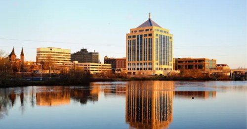 A modern building in a small city rises above the banks of a river.