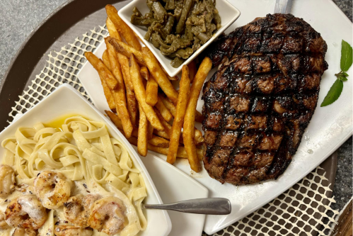 A plate featuring grilled steak, crispy fries, fettuccine with shrimp, and a side of green beans.