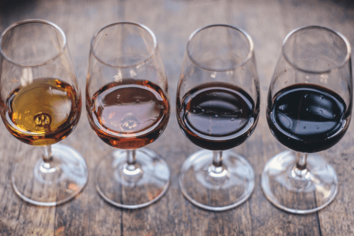 Four wine glasses filled with different colored wines arranged on a wooden surface.