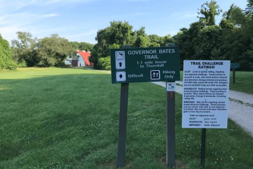Sign for Governor Bates Trail, indicating a 1.1-mile hike to Thornhill, with ratings for trail difficulty. Green landscape in background.