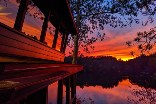 A serene sunset over a lake, with vibrant colors reflecting on the water and a wooden structure in the foreground.