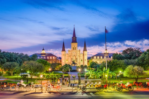 A historic church with a tall spire, surrounded by trees and horse-drawn carriages, under a twilight sky.