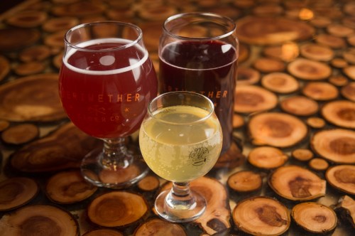 Three glasses of cider in various colors on a wooden table, showcasing a rich, textured surface.