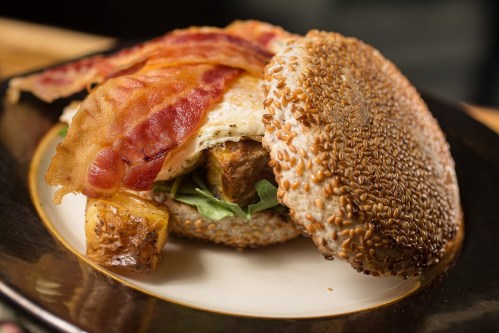 A sesame seed bun filled with bacon, a fried egg, and greens, served on a plate.