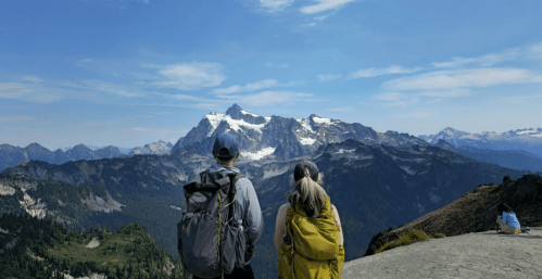 A couple pauses on a mountain peak to look out at the alpine view.