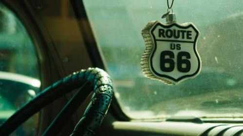 Route 66 trinket hangs from a rear view mirror in a vintage car.