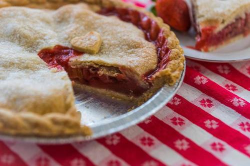 A freshly baked strawberry pie with a slice removed, resting on a red and white checkered tablecloth.