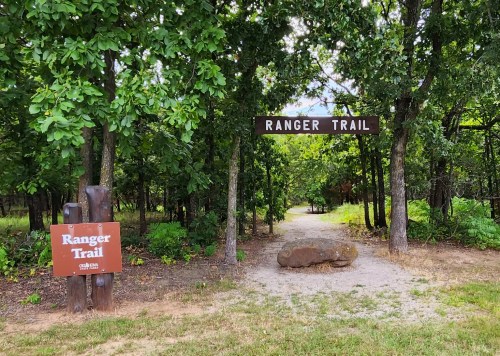 A path marked "Ranger Trail" surrounded by trees, with a signpost on the left indicating the trail entrance.