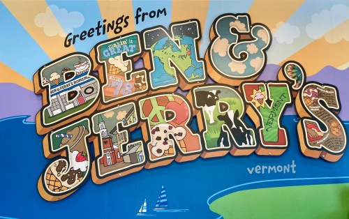 Colorful mural reading "Greetings from Ben & Jerry's Vermont" with ice cream-themed designs and a scenic background.