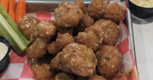 Shiny and well-seasoned deep fried cauliflower served on a checkered paper with celery and carrots.