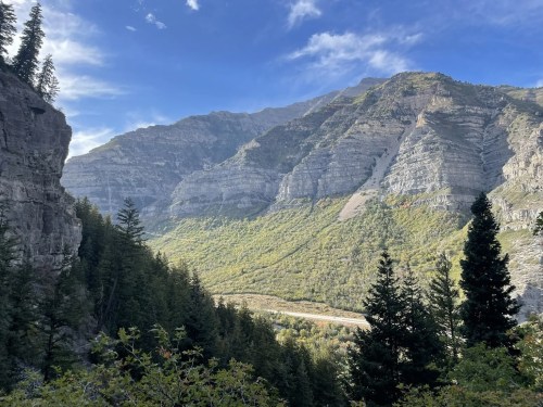 A scenic view of mountains with steep cliffs, lush greenery, and a clear blue sky in the background.