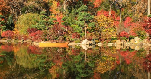 A serene lake surrounded by vibrant autumn foliage, reflecting colorful trees and a wooden boat on the shore.