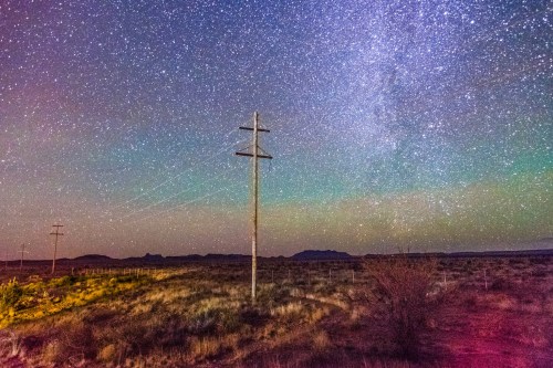 A starry night sky with the Milky Way, featuring a lone power pole in a desert landscape.